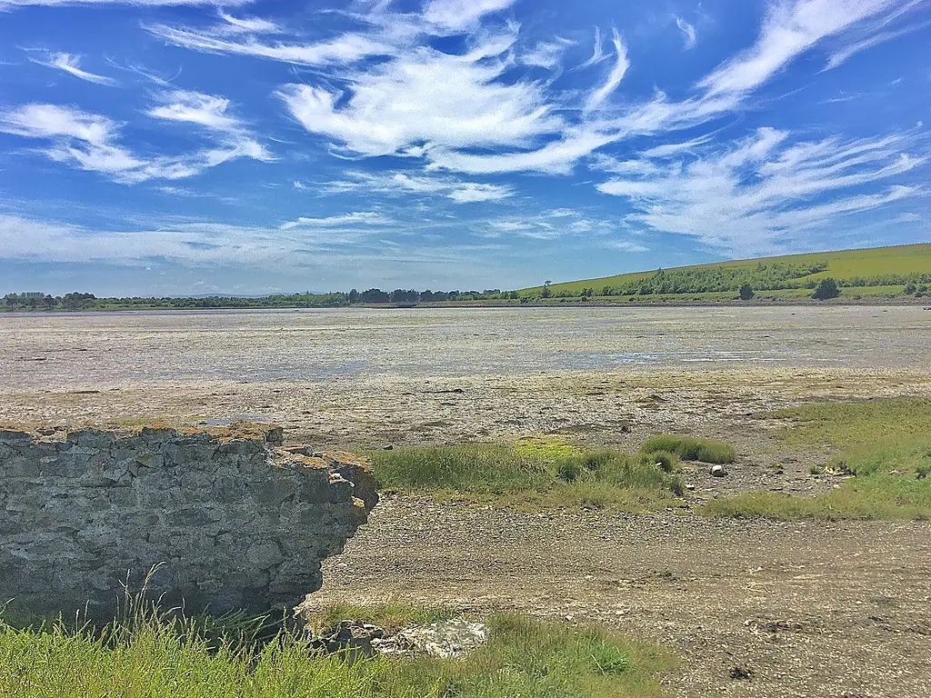 Mudflats of Rogerstown Estuary viewed from the northern side. In the foreground are the remains of an old wall, possibly the remains of an old quayside, while in the distance can be seen the hill of Rogerstown Park